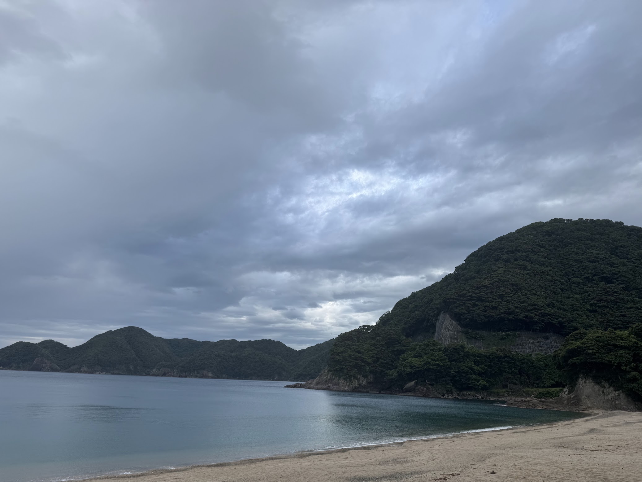 どんより雲の広がる中、べた凪の佐津海水浴場(R8.6.20.夕方撮影)